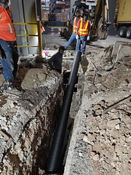 Crew laying a new underground pipe in an excavated trench with an excavator