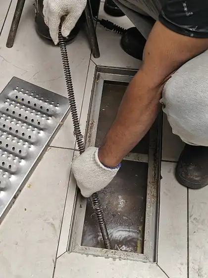 Technician feeding a drain-cleaning spring cable into a blocked floor trap